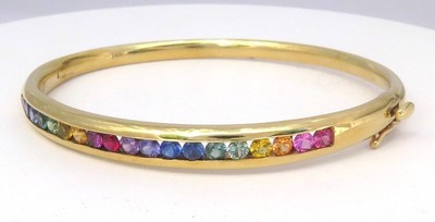 Natural rainbow sapphire bangle bracelet in 14k yellow gold featuring nineteen vibrant sapphires in smooth channel settings.