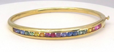 Natural rainbow sapphire bangle bracelet featuring 19 vibrant sapphires set in 14k yellow gold channel settings.