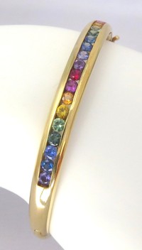 14k yellow gold bangle bracelet featuring 19 vibrant natural rainbow sapphires in smooth channel settings.