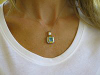 Unique custom blue topaz pendant in 14k white and yellow gold with faceted topaz center and diamond accents.