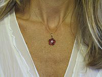 A heart-shaped garnet pendant with diamond accents, set in 14k yellow gold flower design.
