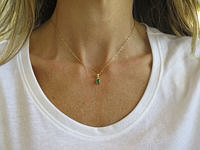 A 14k yellow gold pendant featuring a rich green emerald and three sparkling white diamonds on a fine rope chain.