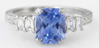 Radiant cut Ceylon sapphire ring with baguette and round diamonds in 18k white gold, featuring intricate hand engraving.